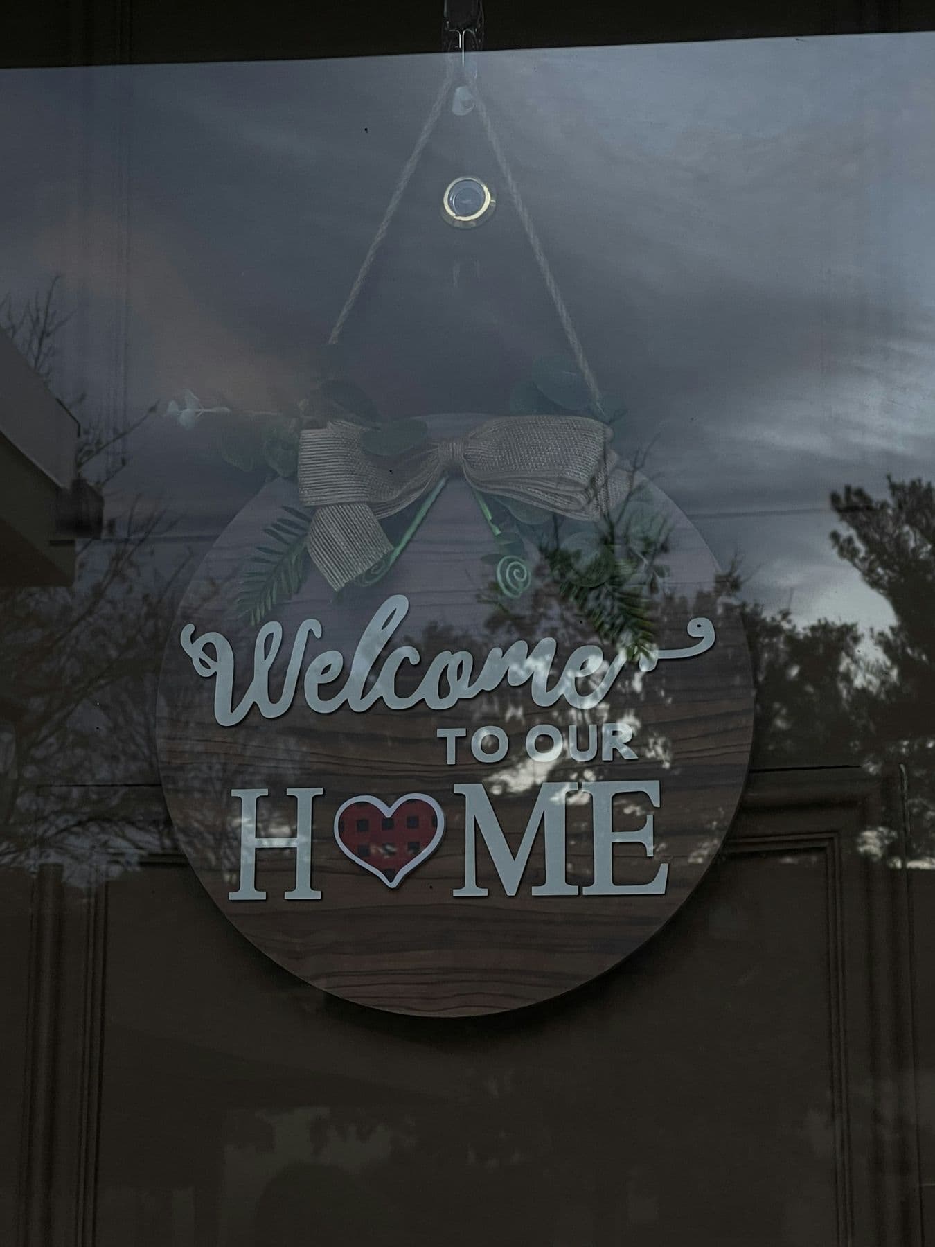A round wooden sign hanging in a window that reads Welcome to our home.